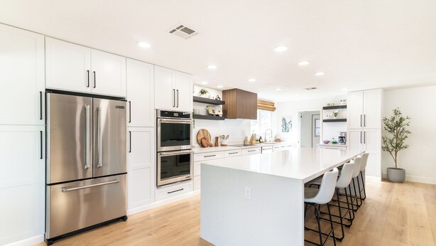 A modern kitchen with white cabinetry, stainless steel appliances, a central island with bar stools, and a potted plant. - Mesa Retreat Quiet, Stylish Desert Escape + Golf (Mesa)
