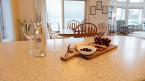 Un coin repas avec une table dressée pour deux personnes, agrémenté d’une bouteille de vin blanc, de verres, d’un bol de raisins et d’une planche en bois avec des amuse-gueules.