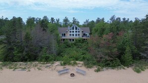 Une grande maison entourée d’une forêt dense, avec une plage de sable au premier plan.