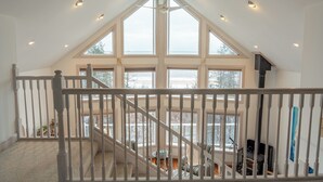 Une chambre spacieuse aménagée en mezzanine, dotée de grandes fenêtres, d’un escalier et d’un coin salon confortable.
