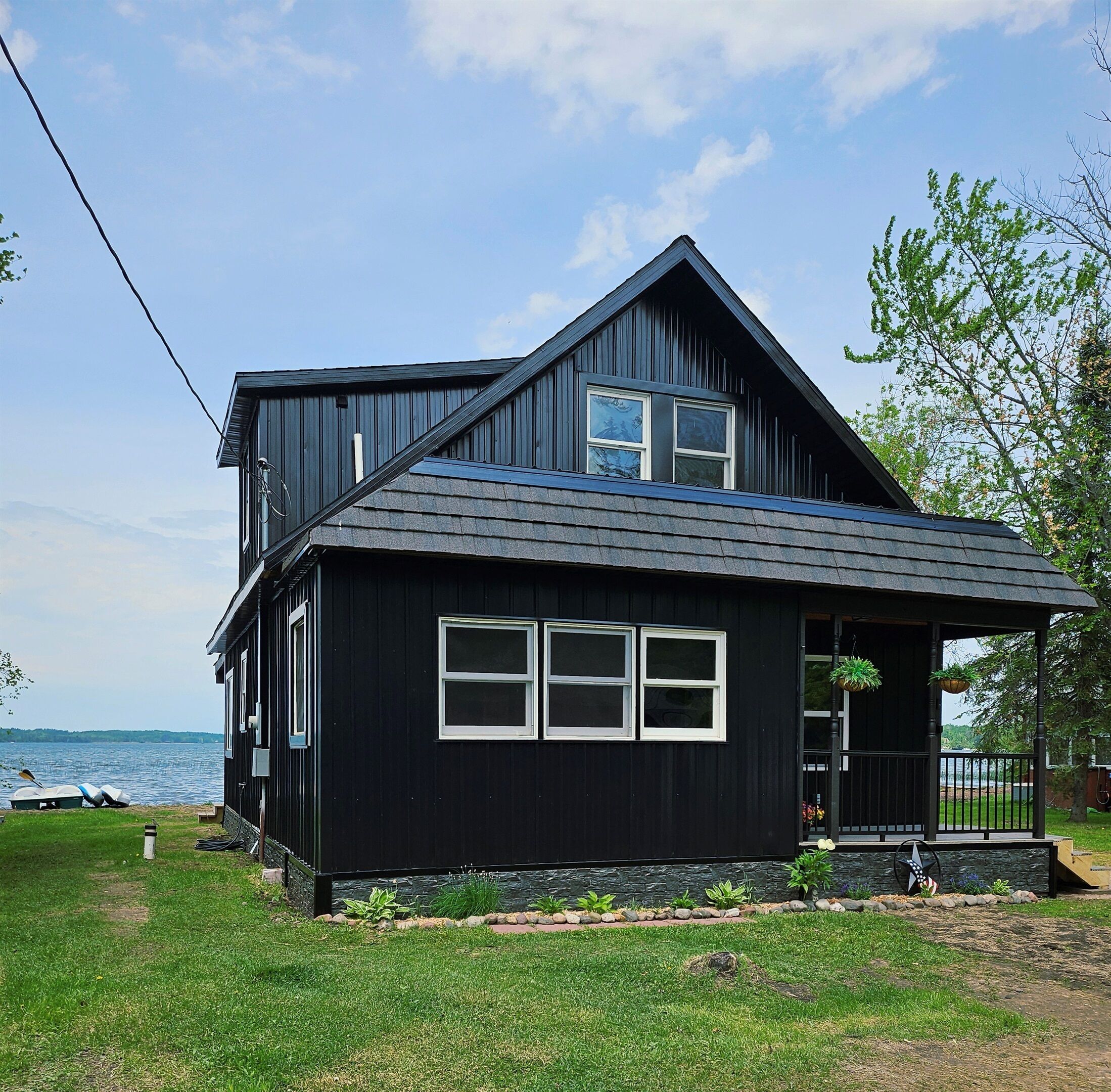 A two-story house with a dark exterior, a sloped roof, and a front porch with hanging planters.