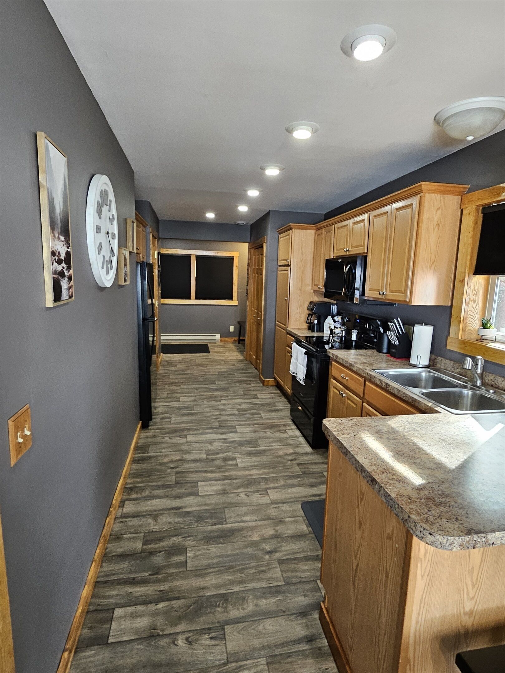 A modern kitchen with wooden cabinets, a granite countertop, and a black refrigerator.