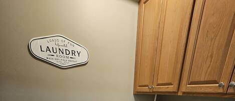 A laundry room with a sign indicating it's a laundry room, a washing machine, a dryer, wooden cabinets, and a tiled floor.