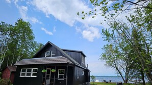 A black two-story house with a front porch, a small garden, and a view of the lake. - Home on Grand Lake, in Saginaw, Near Ivy Black (Saginaw)