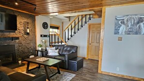 A spacious living room with a fireplace, leather sofa, and a staircase leading to another level. - Home on Grand Lake, in Saginaw, Near Ivy Black (Saginaw)