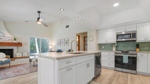 Una cucina moderna con mobili bianchi, un'isola centrale, elettrodomestici in acciaio inossidabile e una ventola a soffitto.