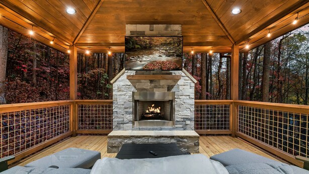 Cómodo espacio al aire libre con chimenea de piedra, terraza de madera y vistas al bosque.