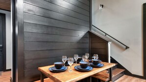 Un comedor con una mesa de madera dispuesta para seis personas, bancos y una escalera.