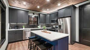 Una cocina moderna con armarios grises oscuros, electrodomésticos de acero inoxidable y techo de madera.