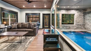 Una sala de estar moderna con un sofá de cuero marrón, una mesa de centro y una zona de piscina con hidromasaje cubierto de cristal.