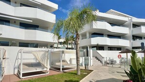 Un edificio moderno con varios balcones, un césped cuidado y zonas de estar al aire libre.