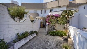 Un patio con un edificio blanco, un muro curvo y un pequeño jardín con plantas y un árbol.