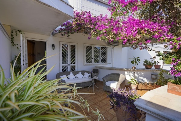 A covered outdoor area with a white wall, two windows, and a sofa.
