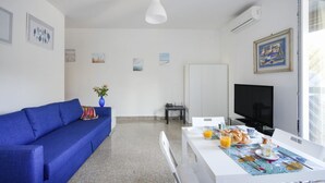 Una habitación moderna con un sofá azul, una mesa de comedor con desayuno, un televisor y obras de arte en las paredes.
