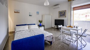 Una habitación de hotel con cama, escritorio, televisión y ventana con cortinas.