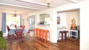 Un comedor amplio con piso de madera, una mesa con sillas y una zona de bar con taburetes.