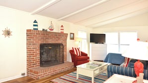 Una sala de estar con chimenea de ladrillo, un sillón rojo, un sofá azul y un televisor sobre un mueble bajo.