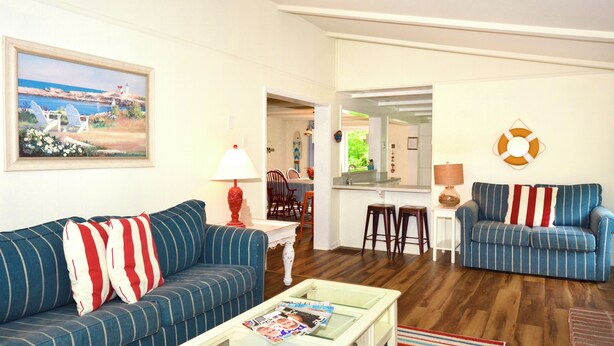 Una sala de estar con sofá, sillones, una mesa de centro y un cuadro de una escena costera.