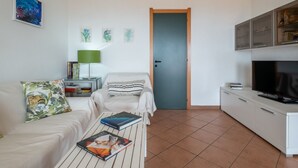 Ein modernes Wohnzimmer mit einer Couch, einem Couchtisch mit Büchern, einem Fernseher und einem Schrank.
