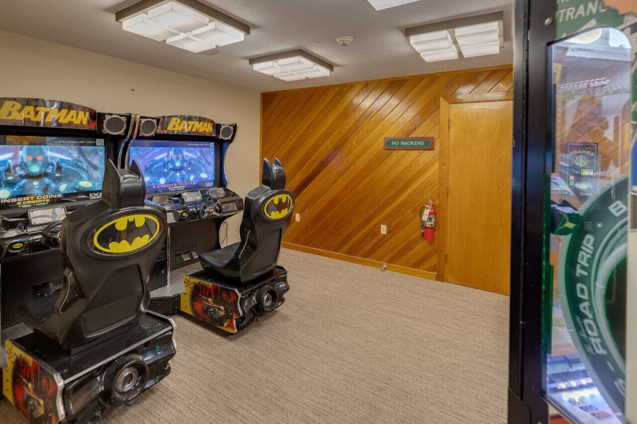 Une pièce avec deux bornes d’arcade sur le thème de Batman, un mur en bois et un panneau « Il est interdit de fumer ».
