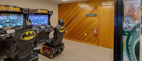 Une pièce avec deux bornes d’arcade sur le thème de Batman, un mur en bois et un panneau « Il est interdit de fumer ».