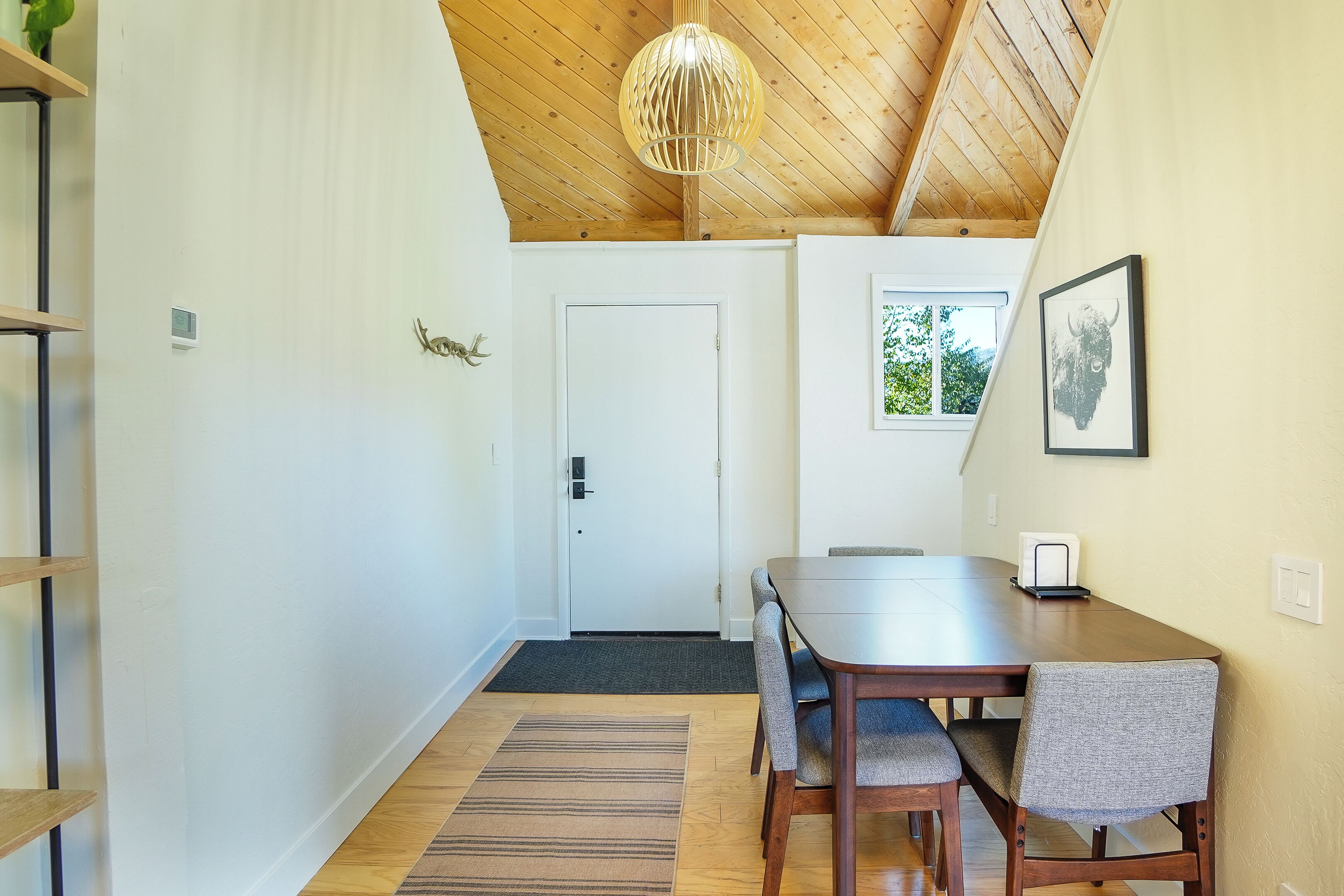 A dining area with a wooden table and chairs, a ceiling light, and a door in the background.