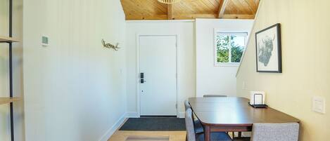 A dining area with a wooden table and chairs, a ceiling light, and a door in the background.