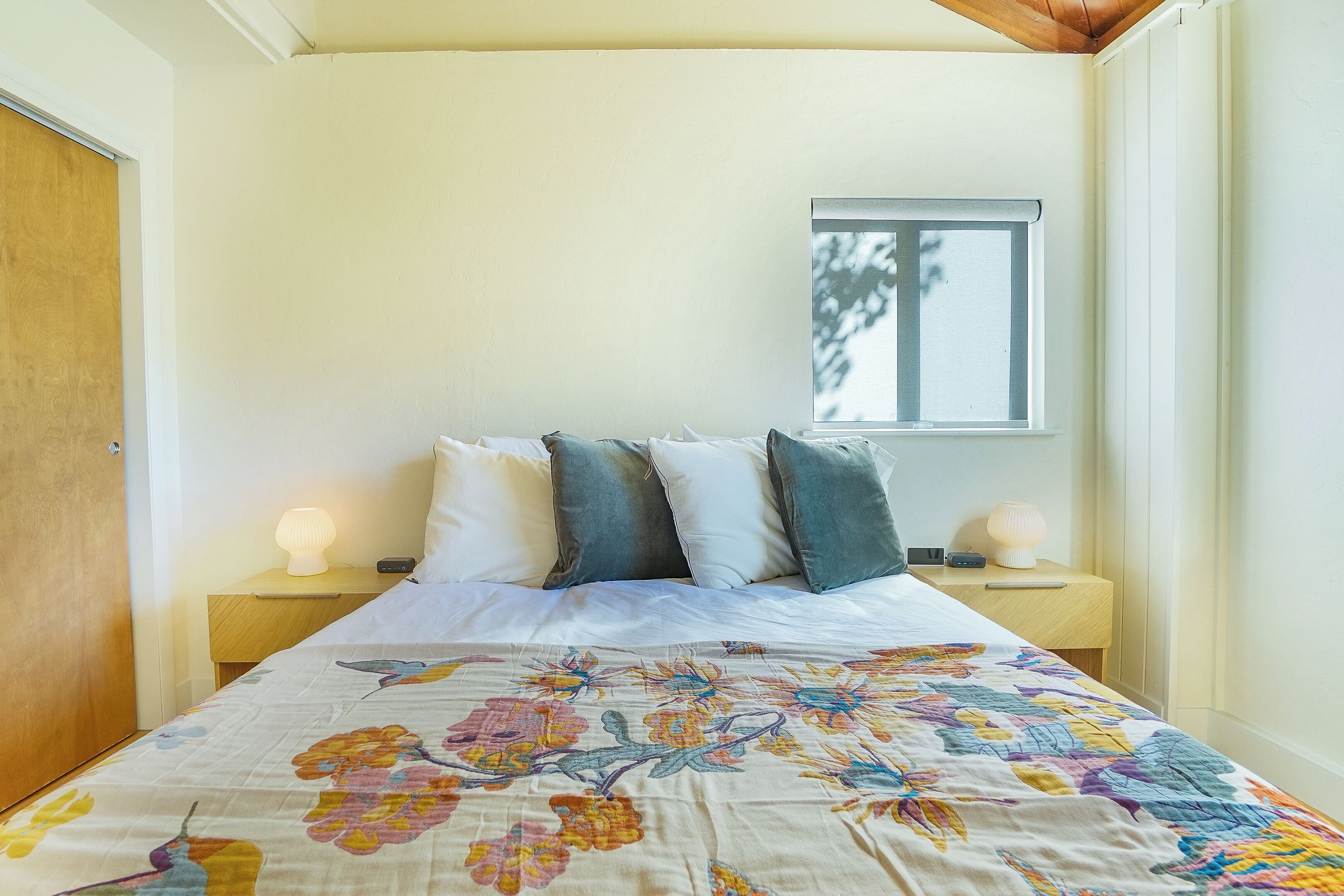 A bedroom with a floral bedspread, a window with a view of trees, and bedside lamps.