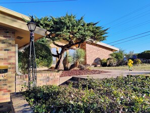 A building with a brick facade, a covered porch, and a tree in the front yard.