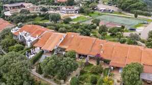 An aerial view of a residential area with terracotta-tiled roofs, lush greenery, and a tennis court. - Le Conchiglie by Interhome (Olbia)