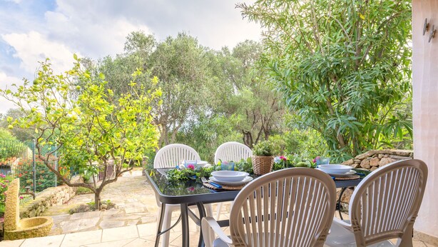 An outdoor patio with a table set for two, surrounded by greenery and trees. - Le Conchiglie by Interhome (Olbia)