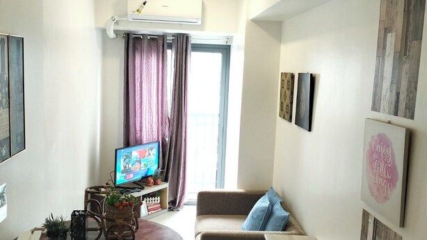 A compact living space with a sofa, a small table with a basket of plants, a television, and a wall-mounted air conditioner. - Cozy Home in BGC (taguig)