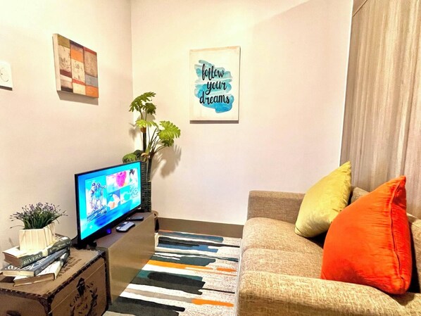 A living room with a television, a sofa with cushions, a plant, and a motivational poster on the wall. - Cozy Home in BGC (taguig)