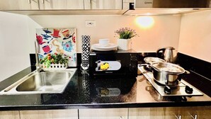 A modern kitchen with stainless steel appliances, a black countertop, and wooden cabinets. - Cozy Home in BGC (taguig)