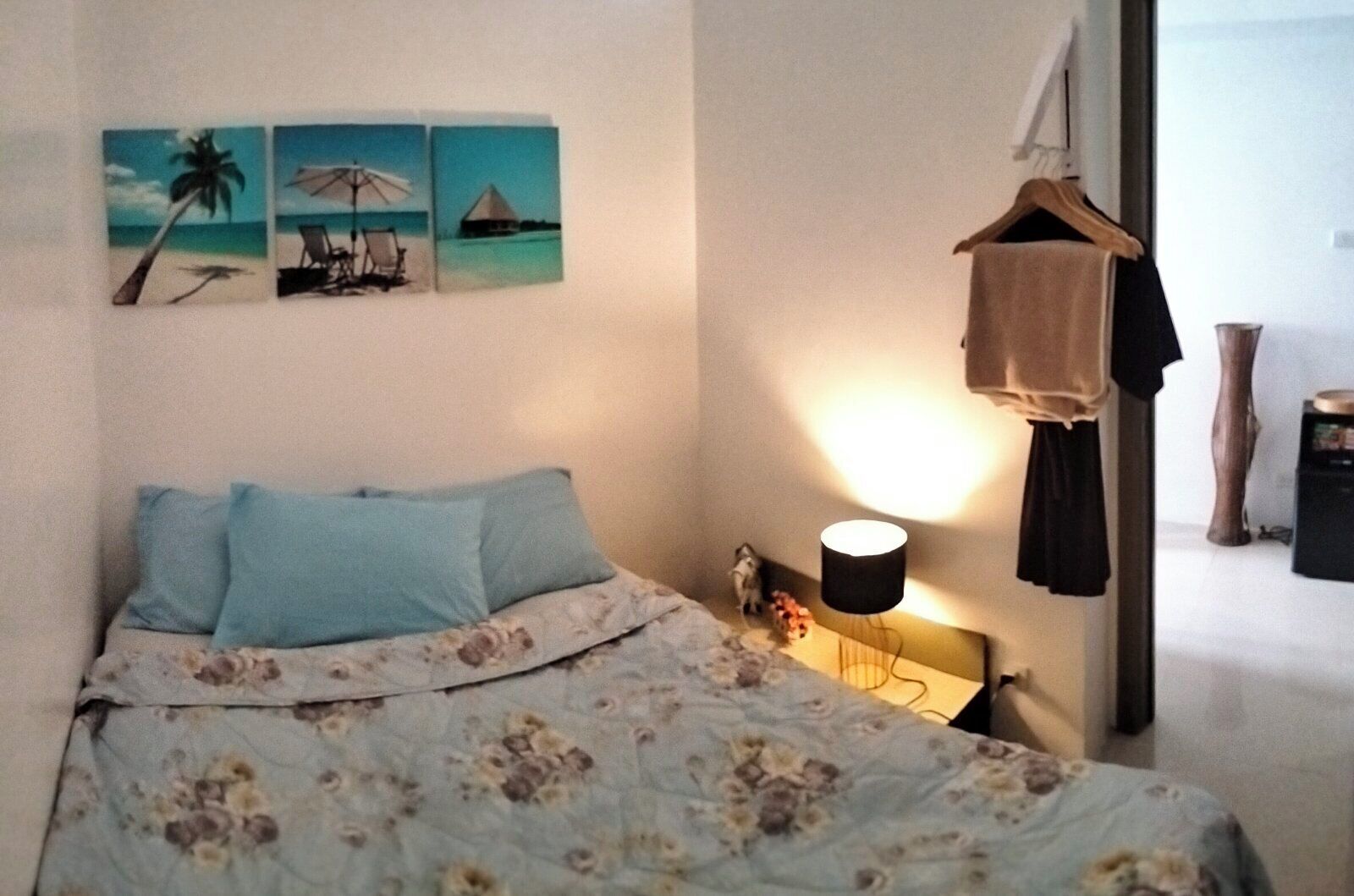 Une chambre à coucher comprenant un lit, une table de chevet, une lampe et des œuvres d’art murales représentant des scènes tropicales.