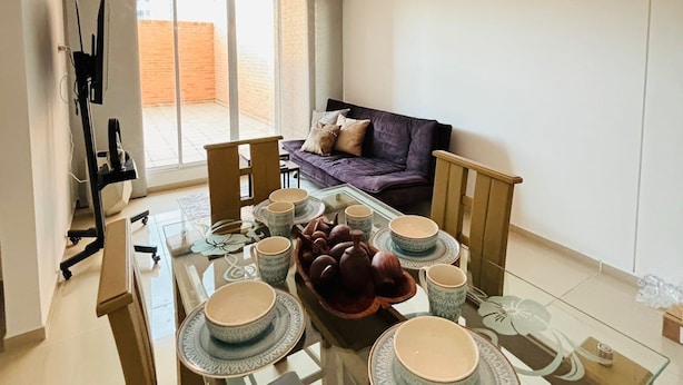 A modern living room with a glass dining table set for four, a sofa, and a ceiling light fixture. - Smart apartment in exclusive area  (Popayán)