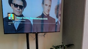 A flat-screen TV mounted on a wall, displaying a music video. Below the TV, there's a small table with a potted plant and a tray with candles. - Smart apartment in exclusive area  (Popayán)