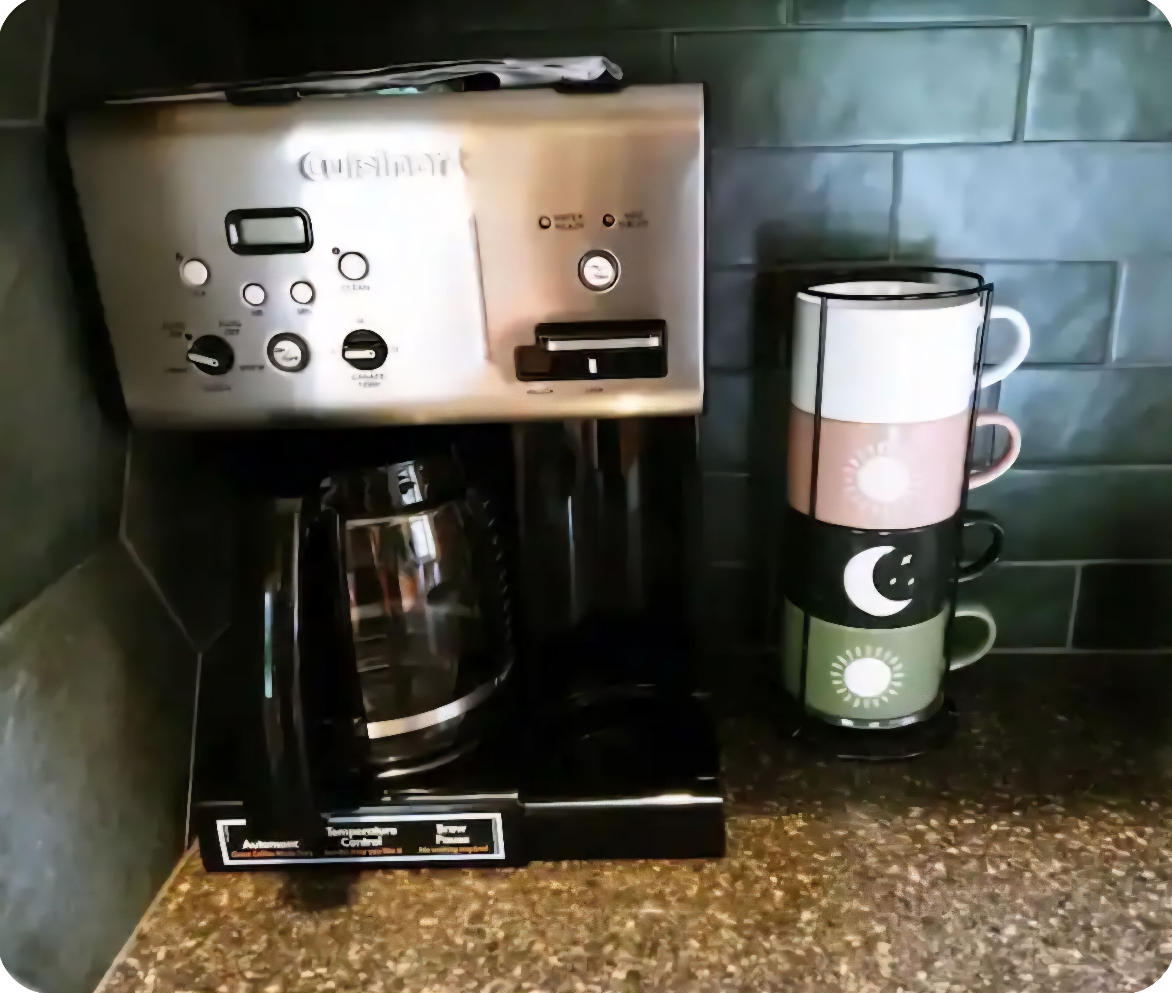 Een koffiezetapparaat met een digitaal display en temperatuurregeling, naast een stapel mokken met een maan- en zonontwerp.