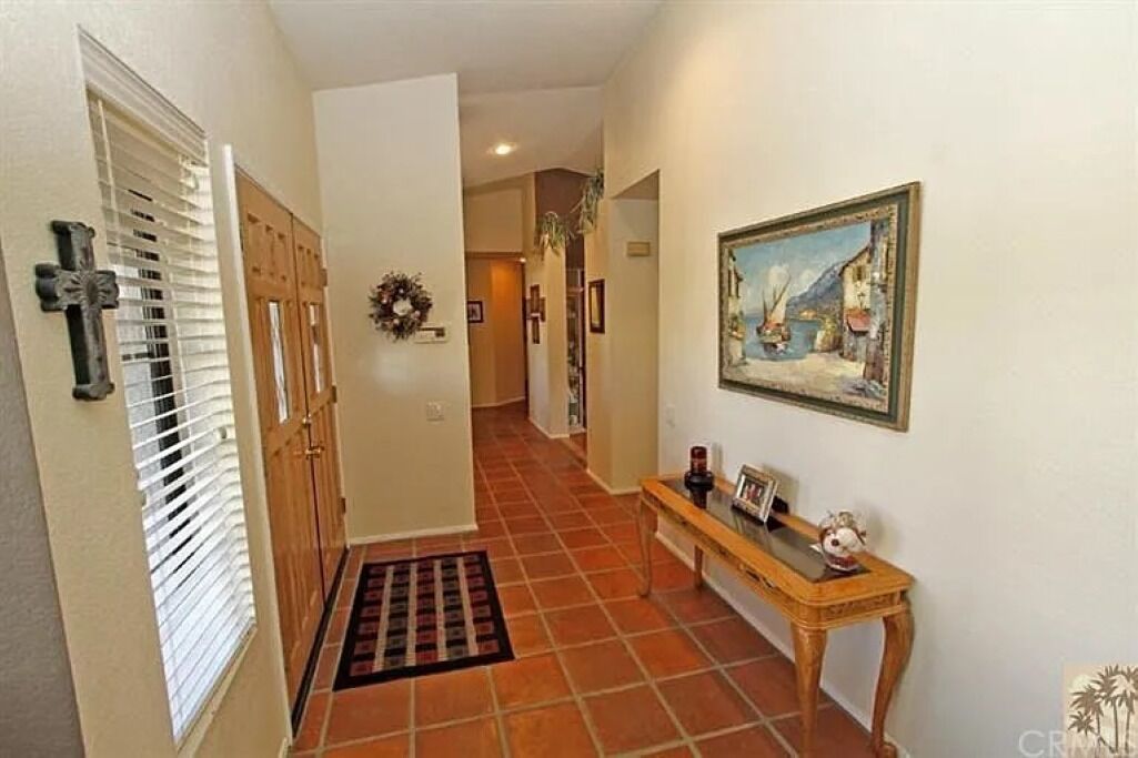 A hallway with a wooden bench, a painting on the wall, and a door with a cross on it.