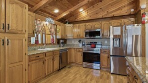 Une cuisine de style rustique, avec des meubles en bois, des plans de travail en granit, des appareils électroménagers en acier inoxydable et un plafond en bois.