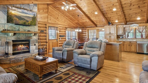 L’intérieur d’une cabane en rondins comprend une cheminée, deux fauteuils, une table à manger et un coin cuisine.