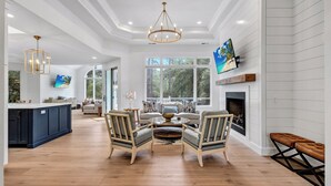 A spacious living room with a fireplace, a large window, and a television mounted on the wall. - Spacious Coastal Getaway | Private Pool, Lagoon Views with Dock, Balcony, and Yard (Hilton Head Island)