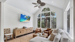 A spacious living room with a large window, a ceiling fan, a television, and a comfortable seating area. - Spacious Coastal Getaway | Private Pool, Lagoon Views with Dock, Balcony, and Yard (Hilton Head Island)