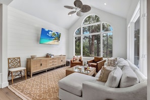 Un salon spacieux doté d’une grande fenêtre, d’un ventilateur de plafond, d’un téléviseur et d’un coin salon confortable.