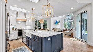 A modern kitchen with a large island, white cabinetry, and pendant lighting. - Spacious Coastal Getaway | Private Pool, Lagoon Views with Dock, Balcony, and Yard (Hilton Head Island)