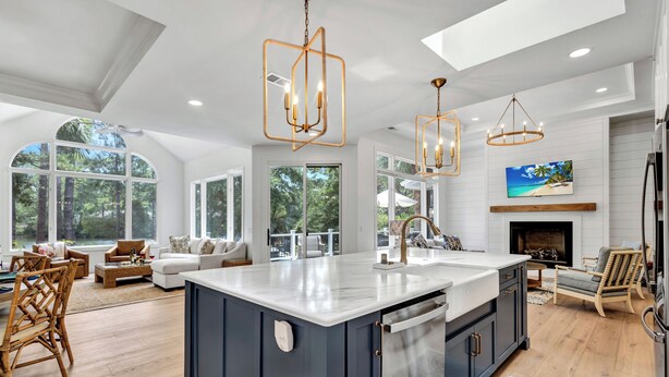 A spacious kitchen with a large island, modern pendant lights, and a view of the outdoors through large windows. - Spacious Coastal Getaway | Private Pool, Lagoon Views with Dock, Balcony, and Yard (Hilton Head Island)