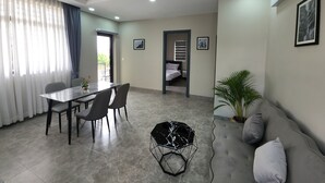 A modern living room with a dining area, a ceiling fan, recessed lighting, a grey sofa, and a potted plant. - My Natural Villas by You Long (Siem Reap)