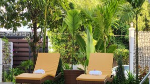 A poolside area with two lounge chairs and a small table, surrounded by lush greenery and a stone wall. - My Natural Villas by You Long (Siem Reap)
