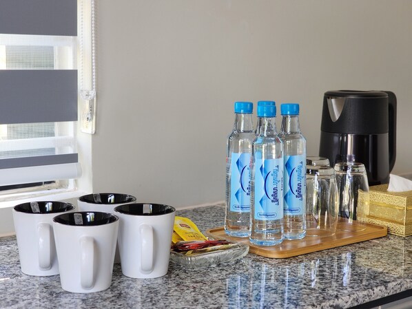 A kitchen counter with four white mugs, three water bottles, a coffee maker, and a tissue box.