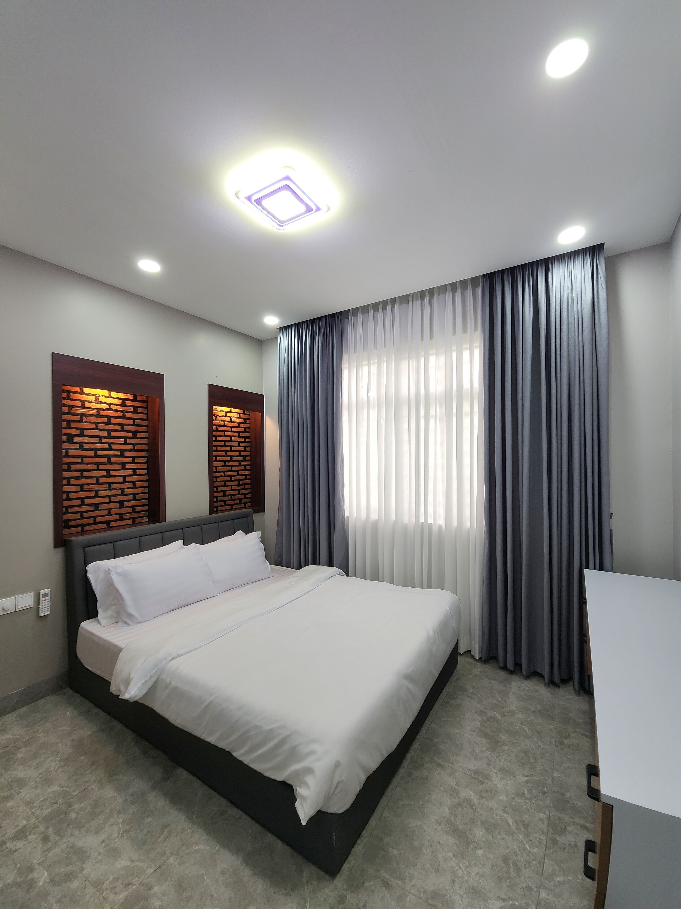 Une chambre d’hôtel moderne avec un grand lit, un bureau et une fenêtre avec des rideaux gris.